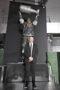 man standing in front of a bronze statue that holds a trophy overhead Dustin Brown of LA Kings
